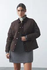 Campera tipo barn capitoneada de color marrón, con silueta corta y relajada. Presenta cuello de pana, cierre frontal con broches metálicos y bolsillos laterales funcionales.