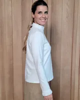 Polera de manga larga color blanco, confeccionada en algodón, con cuello alto tipo tortuga y detalles de volados en el cuello y en los puños.