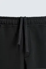 Pantalón jogger de corte relajado y pernera ancha, confeccionado en tejido de algodón con interior perchado. Cuenta con cintura elástica ajustable mediante cordón interior, bolsillos laterales y un bolsillo trasero de plastrón.