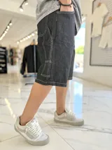 Bermuda baggy de jean negro, con costuras visibles en blanco y diseño holgado.