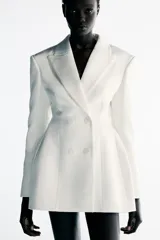 Blazer vestido corto confeccionado en tejido satinado color blanco, con cuello de solapa y cierre frontal cruzado con botones.