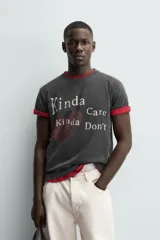 Camiseta de manga corta y cuello redondo, color negro con efecto lavado. Presenta un estampado frontal con un corazón rojo y texto en blanco que dice "Kinda Care Kinda Don't".