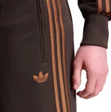 Bermuda Adidas modelo Firebird color marrón, con las clásicas tres tiras en los laterales en tono tostado, bolsillos con cierre y logo del trébol bordado.