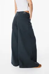 Jean de corte wide leg en color negro lavado, con tiro medio y cierre de botón y cremallera. Presenta bolsillos traseros amplios y etiqueta de cuero sintético con el logo de la marca en la parte posterior.