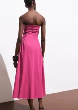 Vestido midi color fucsia, sin mangas, con escote palabra de honor, detalles fruncidos en los laterales del torso y falda evasé.