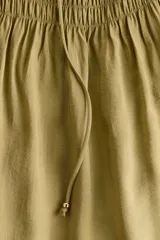 Vestido corto oversized de mezcla de viscosa y color verde militar, con escote en V profundo, cordón ajustable en el cuello y mangas globo largas con puños elásticos. Presenta fruncidos en el canesú y sección de punto smock en la cintura con falda de leve vuelo.