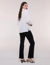 Camisa blanca de corte clásico y caída fluida, con cuello camisero tradicional, abotonadura frontal oculta y mangas largas con puños anchos.