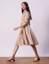 Vestido camisero blanco de algodón con cuello con solapa, delantera abotonada, mangas 3/4 regulables con presilla y botón, y cintura con lazo de ajuste.