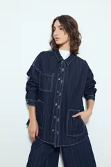 Sobrecamisa de jean color azul oscuro con estampado de rayas verticales blancas. Presenta un corte relajado, cuello clásico, cierre frontal con botones metálicos, mangas largas y dos bolsillos frontales de parche.