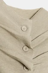 Chaqueta de punto color beige claro, manga larga y cuello redondo. Presenta un detalle de frunces verticales ajustados por botones a tono en el centro frontal.