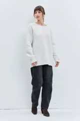 Sweater de punto en color crudo, con diseño de cuello redondo y detalle de bordado sutil en el hombro derecho. Presenta un corte holgado y mangas largas con puños acanalados.