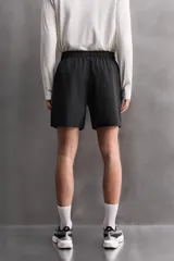 Pantalones cortos deportivos color marrón rojizo, confeccionados en tejido técnico ligero y elástico. Presentan cintura elástica ajustable con cordón interior, bolsillos frontales y un bolsillo trasero con cierre de cremallera. Los laterales tienen perforaciones para transpirabilidad y aberturas laterales en el bajo.