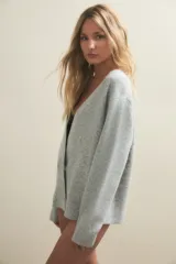 Cardigan de punto gris claro, con escote en V profundo, cierre frontal cruzado con botones y mangas largas holgadas.