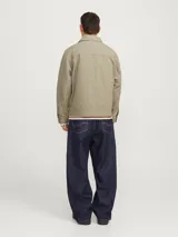 Campera estilo worker de corte recto, confeccionada en tejido plano Oxford de algodón color verde grisáceo. Presenta cuello clásico, cierre frontal completo con cremallera metálica, mangas largas con puños abotonados y bolsillos laterales integrados.