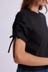 Remera negra de manga corta con cuello redondo y fruncidos ajustables mediante cordones en las mangas.