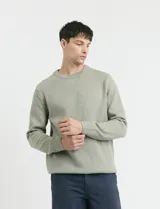 Sweater de punto en color verde claro, con cuello redondo y mangas largas. Presenta un diseño clásico de tejido liso con puños y ruedo acanalados.