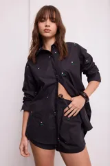 Camisa negra de algodón con bordados de pequeñas flores rosas. Presenta cuello clásico, cierre frontal con botones y mangas largas.