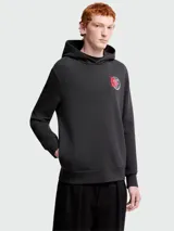 Buzo con capucha Moncler, color negro, de corte regular, con bolsillo frontal tipo canguro y parche circular con logo de la marca en el pecho.