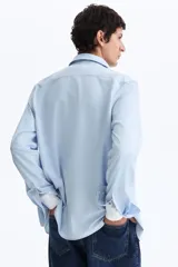 Camisa de manga larga en tejido elástico de mezcla de algodón, con cuello italiano, cierre frontal de botones y puños ajustables. Presenta un corte entallado slim fit y bajo redondeado.