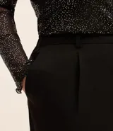Pantalón zanahoria de vestir negro, con cintura alta, elástico en la espalda, bolsillos laterales, botón metalizado y pliegues delanteros.