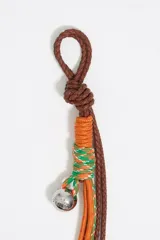 Colgante para bolso con cordones de cuero marrón, cordones trenzados naranja y verde, y dije metálico plateado.