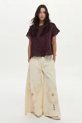 Blusa de lino color beige, de manga corta con volados, cuello redondo y espalda cruzada con volados.