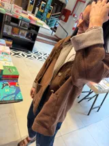 Campera de paño color marrón con diseño de botones frontales, bolsillos laterales y puños con vuelta en tejido de espiga bicolor. Presenta un corte holgado y estructura clásica.