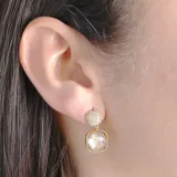 Aros colgantes dorados con base circular cubierta de circonias y un dije cuadrado con incrustaciones de cristal.