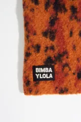Balaclava de punto con diseño envolvente, confeccionada en tejido texturizado con estampado animal print tipo lince en tonos naranja, rojo y negro. Presenta cordones ajustables en el cuello y etiqueta con logo de la marca en la parte inferior.
