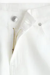 Jean de cinco bolsillos en denim rígido, de color blanco, con piernas amplias, corte holgado y cintura estándar con cierre y botón.