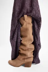 Bota de caña alta confeccionada en cuero vacuno, con diseño versátil que permite doblar la caña. Presenta un taco cuadrado de altura media y punta redondeada.