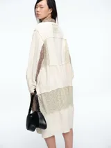 Vestido camisero de corte midi con diseño patchwork que combina paneles en tonos crudo y marrón con estampados florales sutiles. Presenta cierre frontal con botones, cuello camisero y mangas largas con puños.