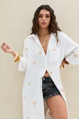 Camisola larga color blanco crudo, de manga larga, con cuello camisero, bolsillo frontal en el pecho y diseño abotonado. Presenta pequeños bordados distribuidos en toda la prenda.