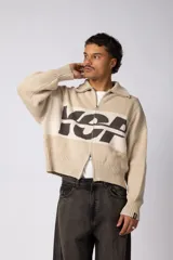 Campera tejida de punto con cierre frontal completo y cuello polo. Presenta un diseño con franja horizontal en color azul y letras en blanco sobre fondo negro, con puños y ruedo acanalados.