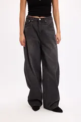 Pantalón de jean estilo baggy, de corte amplio y tiro medio, confeccionado en denim negro con textura de pana fina. Presenta diseño de cinco bolsillos, cierre frontal con botón metálico y cremallera, y perneras holgadas.