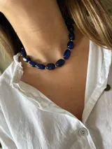 Collar corto compuesto por piedras ovaladas de color azul profundo, intercaladas con pequeñas cuentas plateadas. Está confeccionado en acero quirúrgico e incluye una cadena de alargue para ajustar el largo deseado.