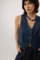 Chaleco de denim azul con cuello en V, cierre frontal con botones metálicos y pespuntes en contraste.