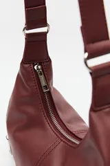 Cartera de hombro color bordó, de símil cuero, con diseño curvo y detalles de cierres metálicos en los extremos.
