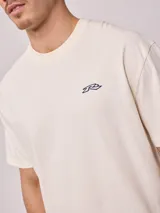 Remera de algodón con lavado, color crema o blanco roto, de corte regular fit y manga corta. Presenta un pequeño logo bordado en el pecho.