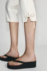 Pantalón capri de tiro alto en color crudo, con detalle de lazos ajustables en los bajos y cierre lateral con cremallera oculta.