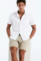 Camisa de manga corta color blanco en popelina, con cuello clásico, cierre frontal con botones y bolsillo aplicado en el pecho.