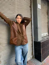 Chaqueta de punto color marrón con cuello de punto acanalado y solapas de cuero. Presenta un cinturón de tela con hebilla dorada y bolsillos de cuero con detalles de cordones.