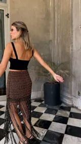 Falda corta tejida a mano en crochet, con diseño a rayas horizontales en tonos marrón oscuro y dorado brillante. Presenta un borde inferior con flecos largos y abundantes.
