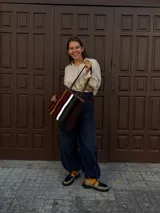 Cartera tipo tote de cuero con diseño de franjas verticales multicolores en tonos tierra, rojo y azul. Cuenta con correas trenzadas de cuero y cierre superior.