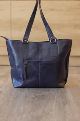 Cartera tote de cuero genuino color azul marino, con doble asa de hombro, costuras verticales y detalle de borla de flecos colgante.