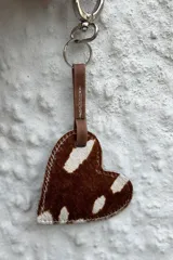 Llavero con dije en forma de corazón confeccionado en cuero con pelo estampado tipo animal print, con tira de sujeción de cuero liso y gancho metálico.