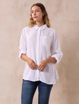 Camisa blanca de lino con cuello con solapa, manga larga regulable con presilla y botón, y abertura central con botones.