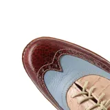 Zapato tipo Oxford de cuero color beige con detalles en charol negro y blanco, con cordones negros y taco bajo de madera.