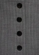 Chaleco de corte crop y diseño recto con cuello en pico y cierre frontal de botones. Presenta un estampado de raya diplomática y cuenta con forro interior y detalle de cinta en la parte posterior.