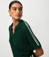 Blusa femenina de punto color verde oscuro, con cuello polo y abertura delantera sin botones. Presenta una trama ahuecada con textura uniforme y mangas cortas con detalle de rayas blancas en los hombros. El modelo es recto y de largo regular.